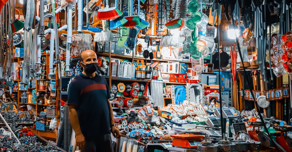 A man wearing a black facemask standing in a crowded hardware store filled with various tools and merchandise.